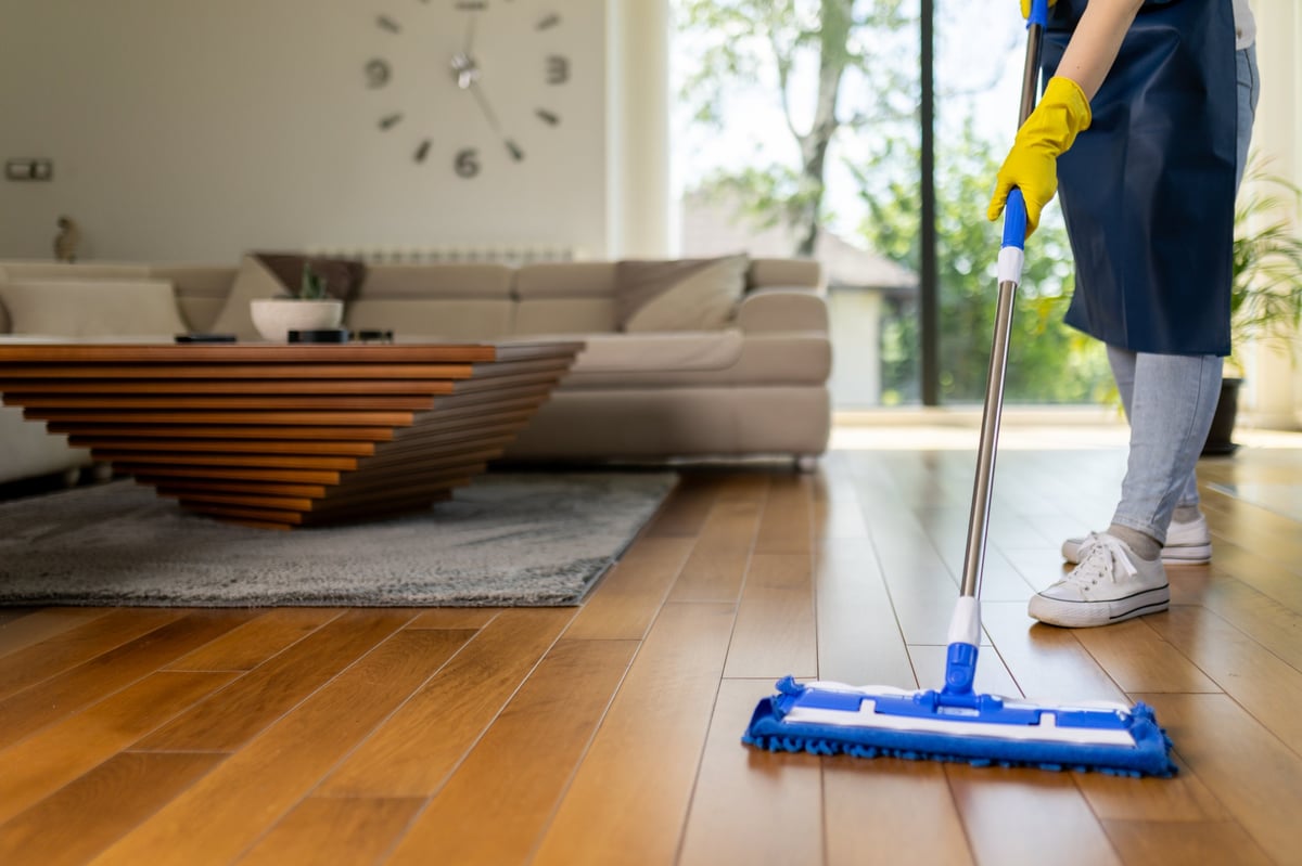 Professional cleaner mopping hardwood floors in a bright home